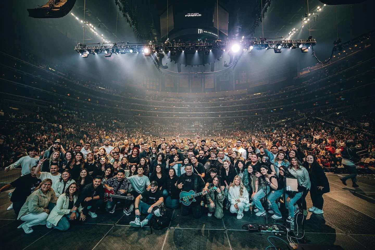Foto de grupo en el escenario de una arena llena, con el público detrás