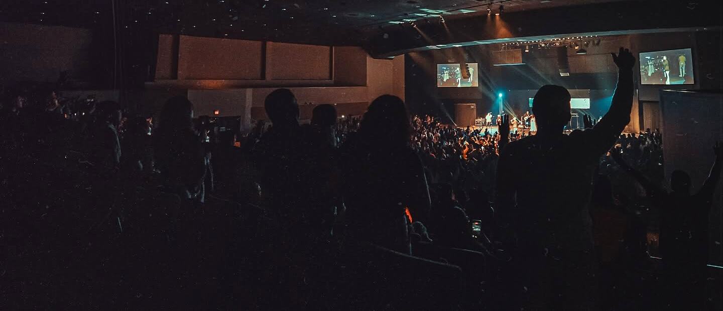 Público con las manos en alto en un auditorio a oscuras, frente al escenario